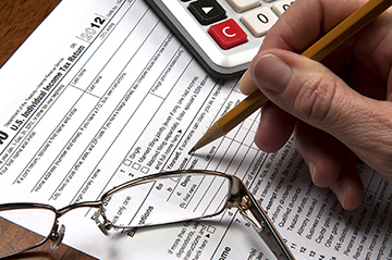 View of United States tax form with hand holding sharpened pencil with calculator and glasses